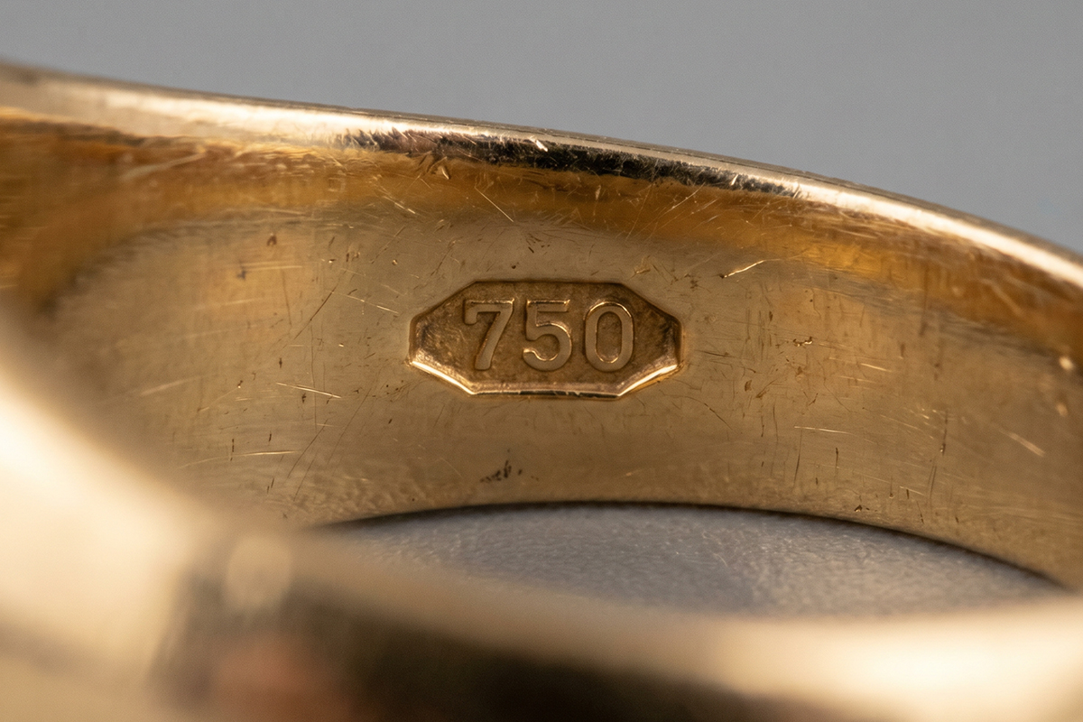 Close-up of the inside of a gold ring band showing the 750 hallmark in an octagonal cartouche, certifying 18K gold purity