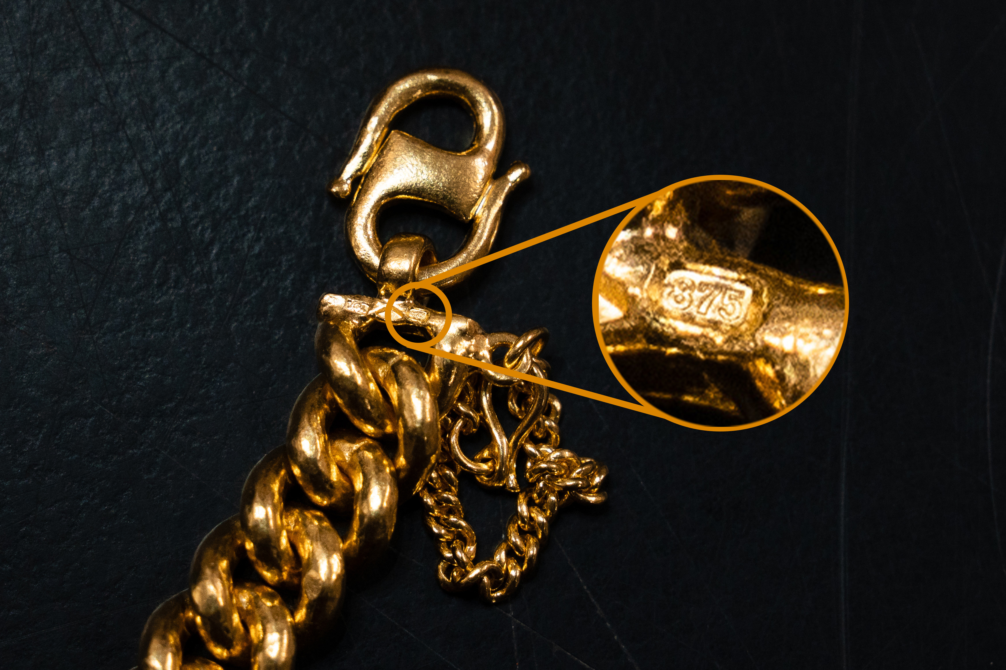 Close-up of a gold chain clasp with a magnified inset showing the 875 hallmark, the fineness stamp for 21K gold