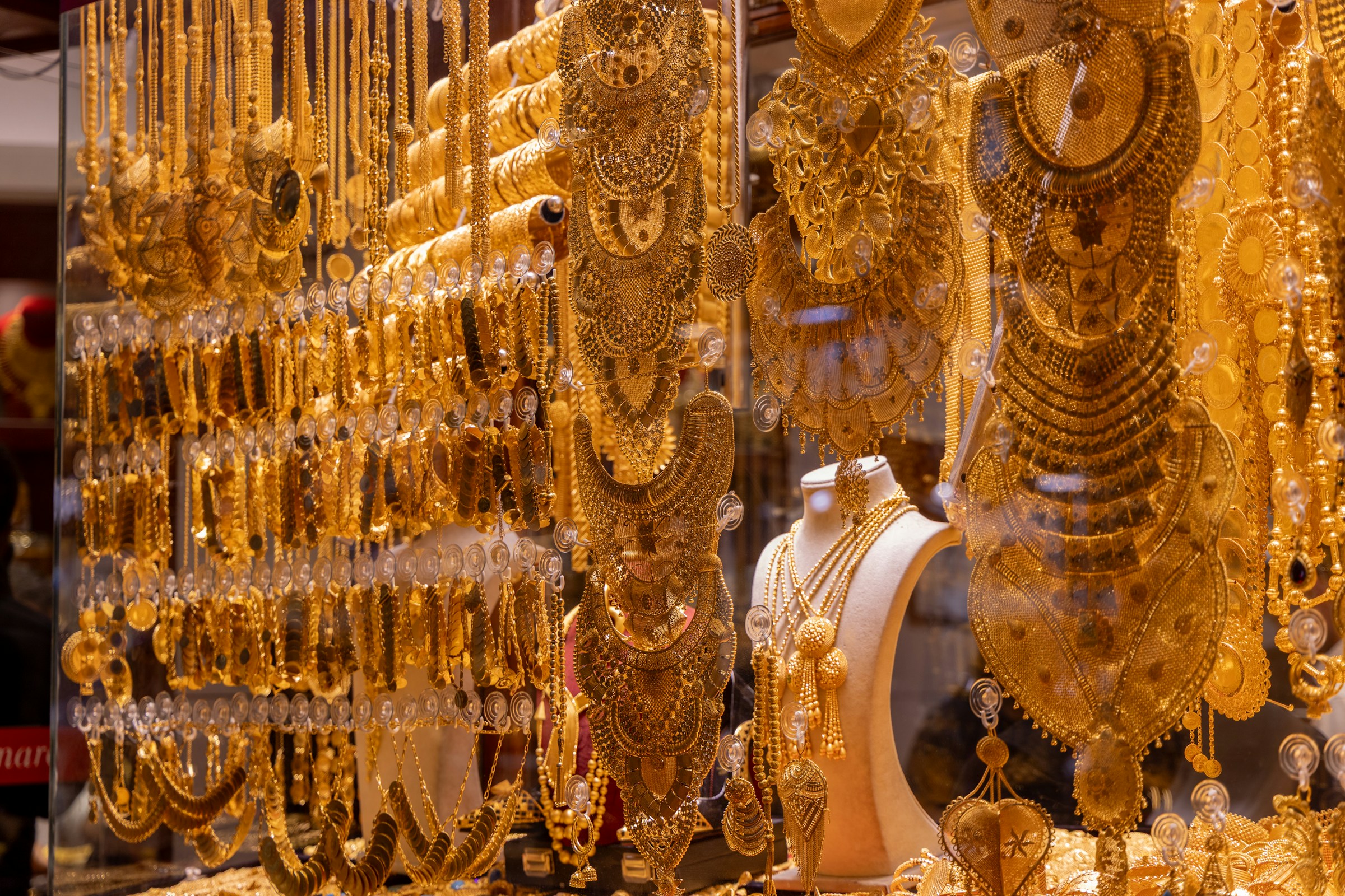 Dense display of intricate yellow gold necklaces and bridal sets hanging in the window of a Middle Eastern gold souk