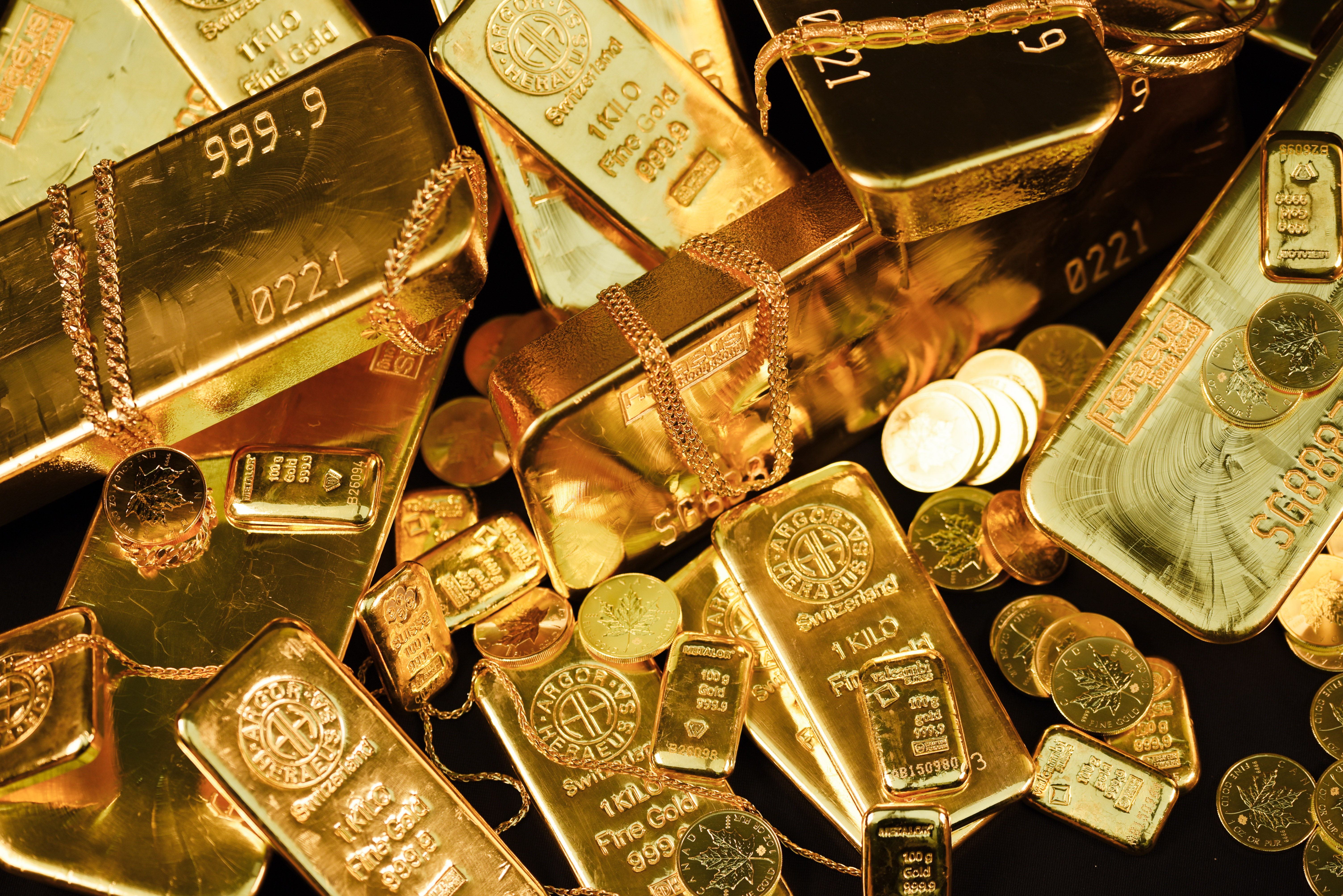Pile of 24K gold bars, coins, and chains stamped 999.9 fine gold, including kilo bars and minted bars from Argor-Heraeus and Metalor