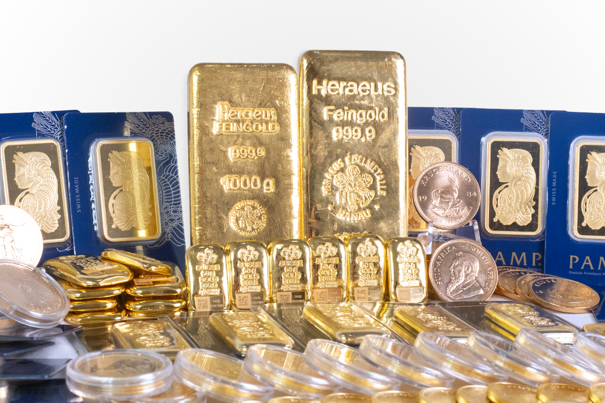 Heraeus 1000g cast gold bars standing behind PAMP minted bars and gold bullion coins including a Krugerrand