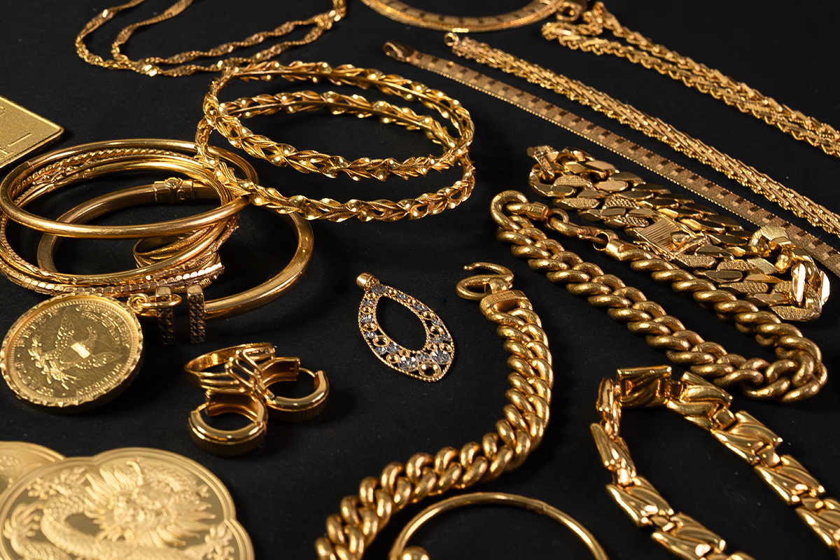 Collection of yellow 24K gold jewelry on a black background, including chain necklaces, bangles, bracelets, and a gold coin