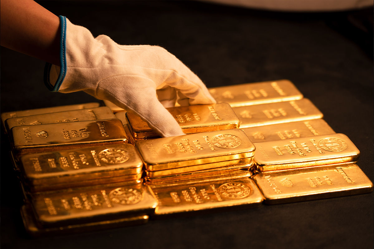 White-gloved hand resting on a neatly stacked pile of one-kilo gold bullion bars