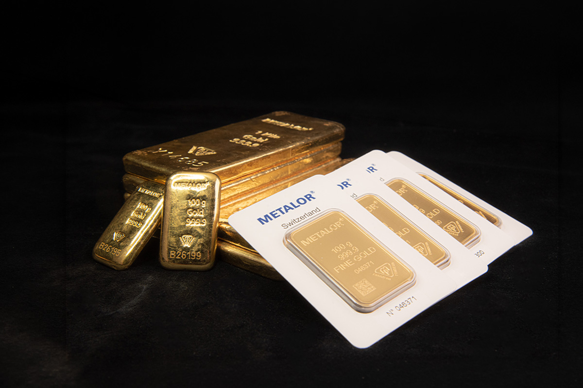 Cast gold bars stacked behind packaged 100-gram Metalor minted gold bars on a black background