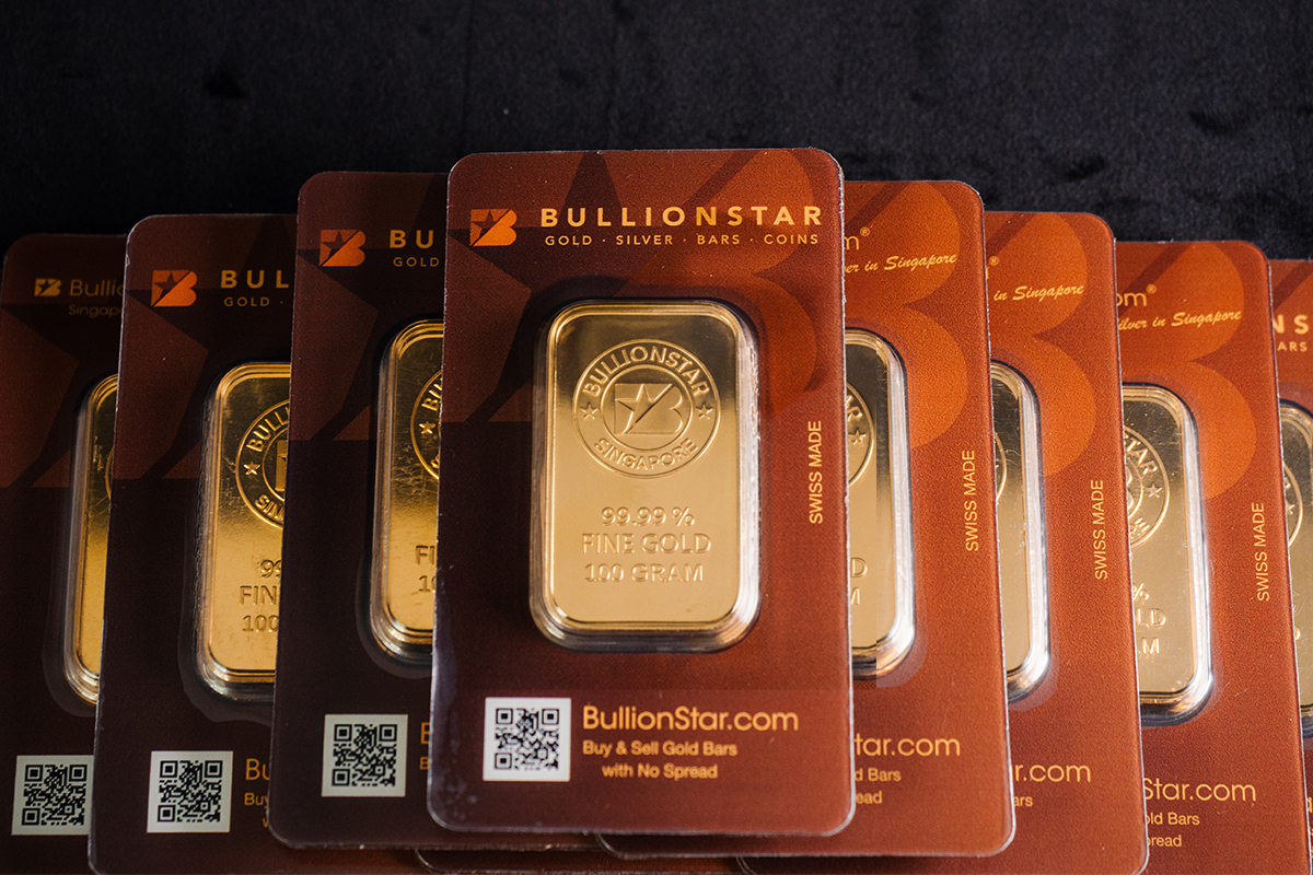 Row of sealed BullionStar 99.99% fine gold 100-gram bars in branded certified packaging