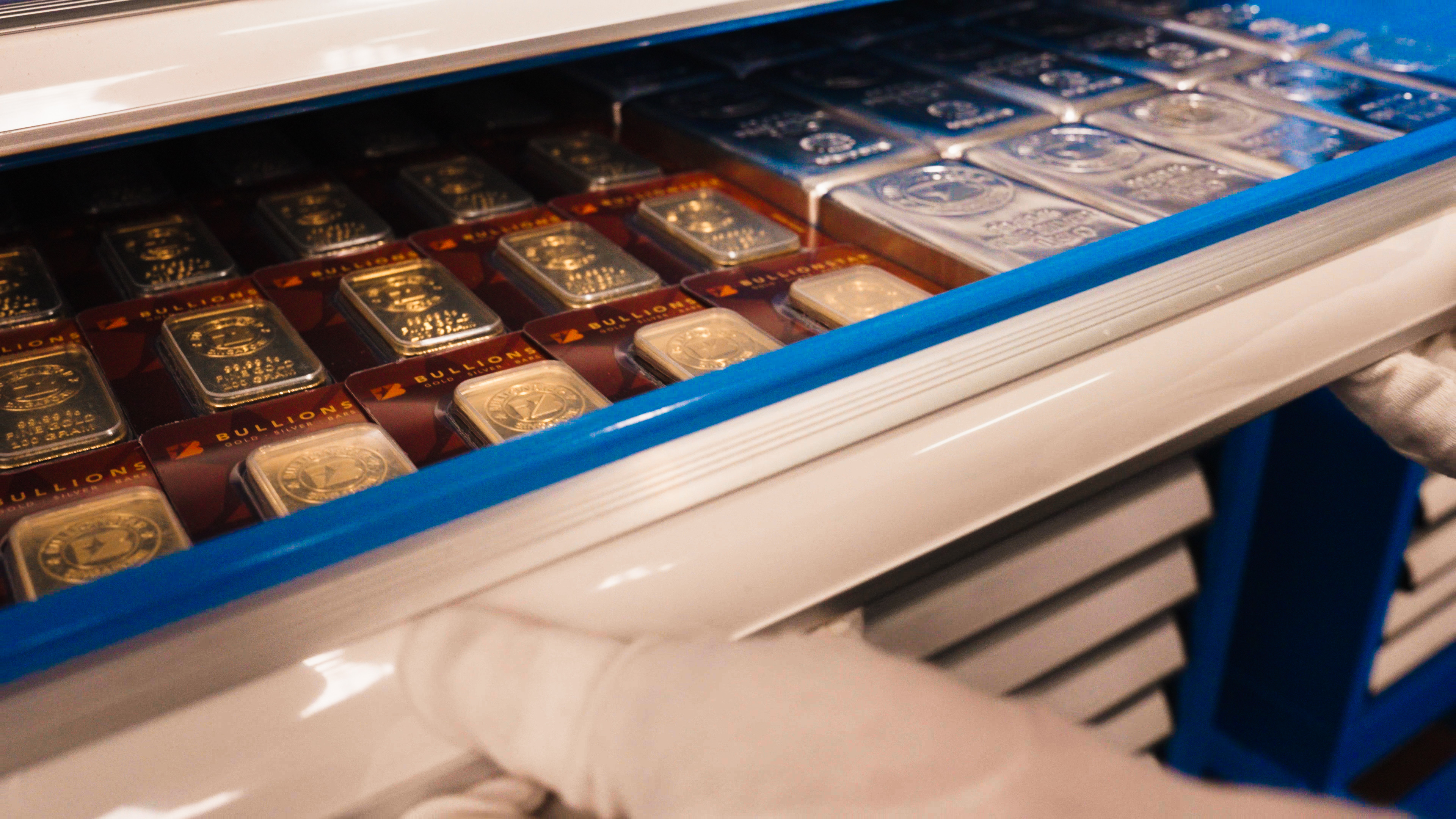 Gloved hand opening a storage drawer of BullionStar-packaged gold and silver bars inside a secure vault