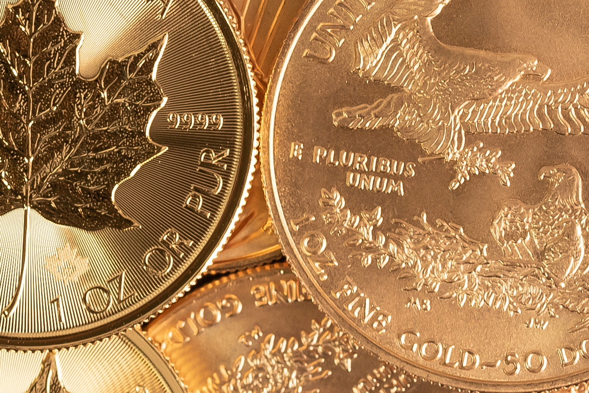 Close-up of a 1 oz Canadian Gold Maple Leaf and a 1 oz American Gold Eagle coin, with "1 OZ" weight specifications visible on both