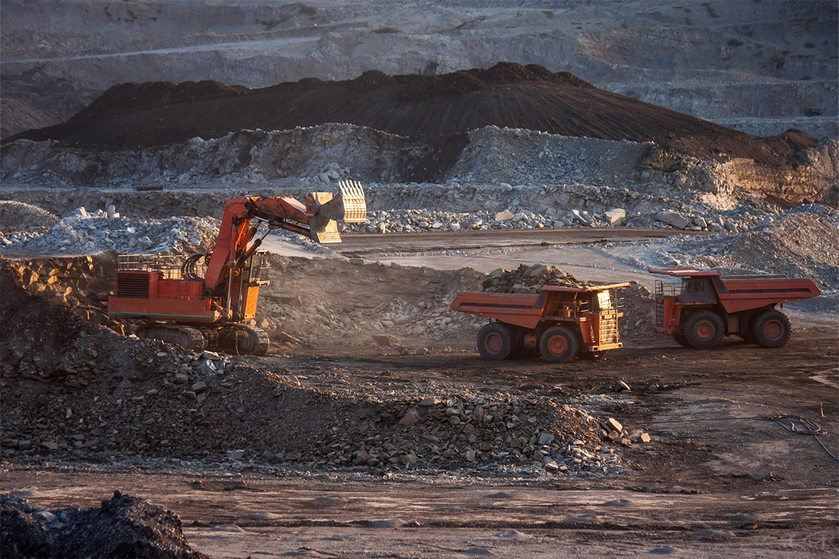 Excavator and haul trucks working an open-pit mine at dusk, representing gold mining operations