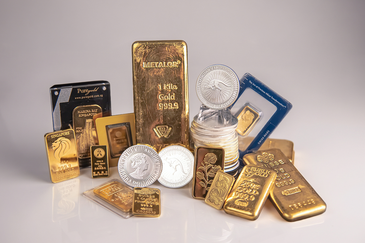 Collection of gold and silver bullion bars and coins on a clean studio backdrop, including a Metalor 1kg gold bar, Singapore Lion and Marina Bay bars, PAMP bars, and Australian Kangaroo coins