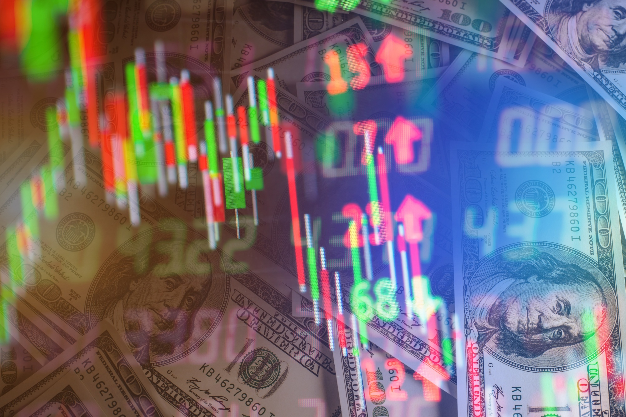  US hundred-dollar bills overlaid with a volatile candlestick stock chart in red and green