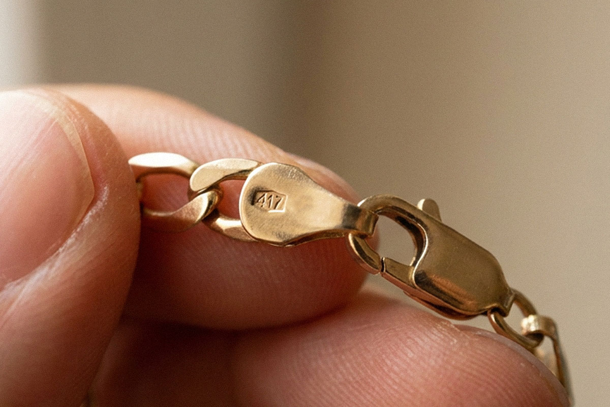 Close-up of a gold chain clasp held between two fingers, showing a "417" hallmark stamp