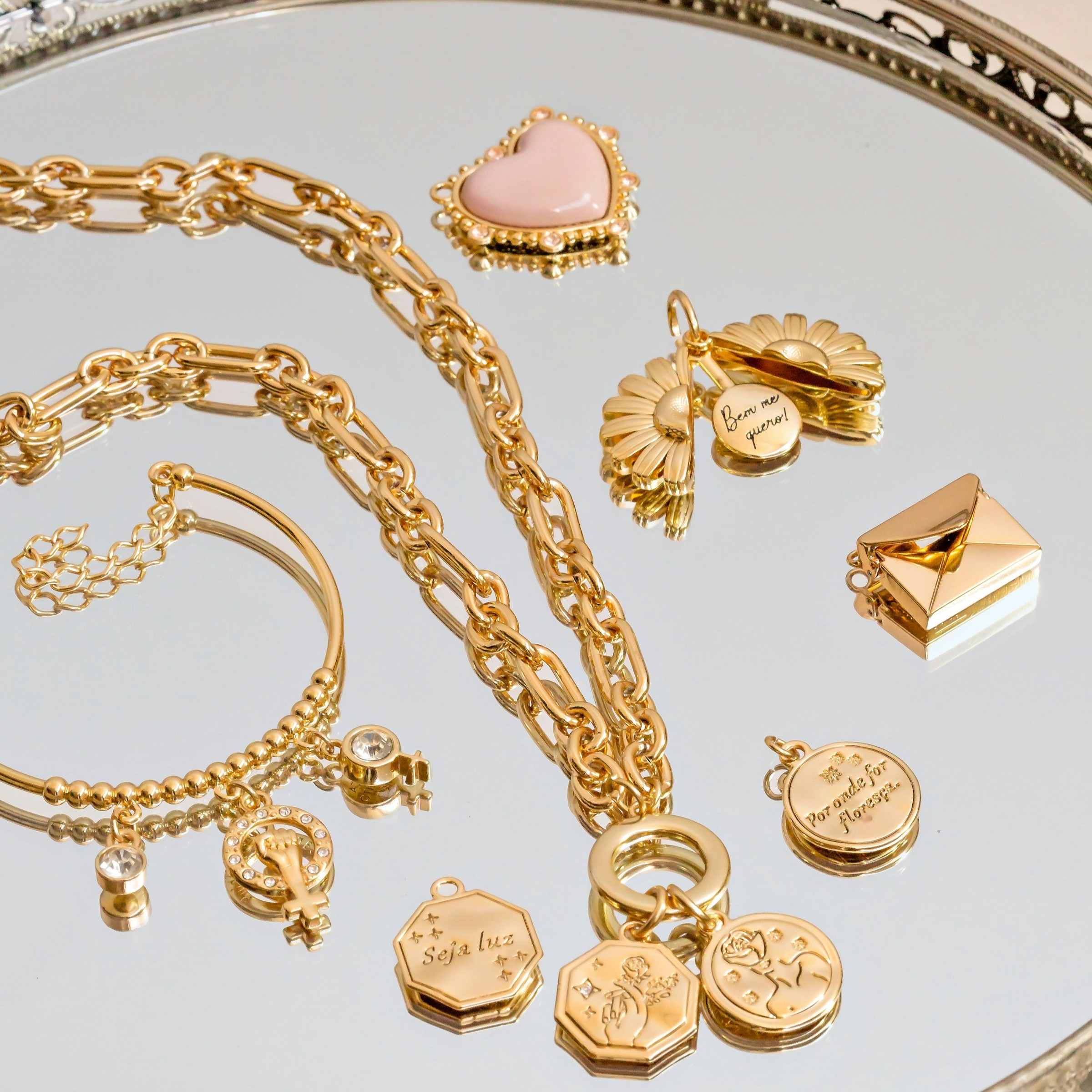Assorted gold jewelry pieces including chain necklaces, a bangle bracelet, and charm pendants arranged on a mirrored tray