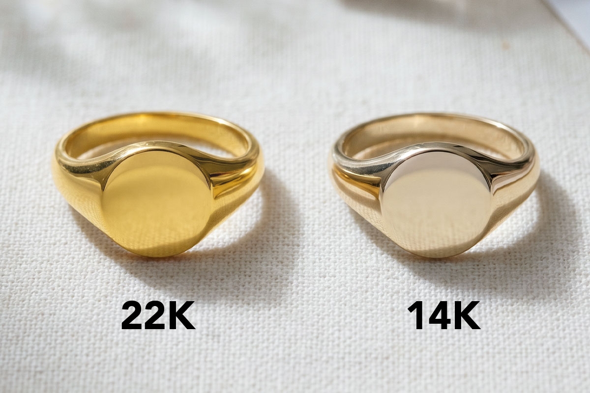 Side-by-side comparison of a deeper yellow 22K gold signet ring and a paler 14K gold signet ring, labelled "22K" and "14K"