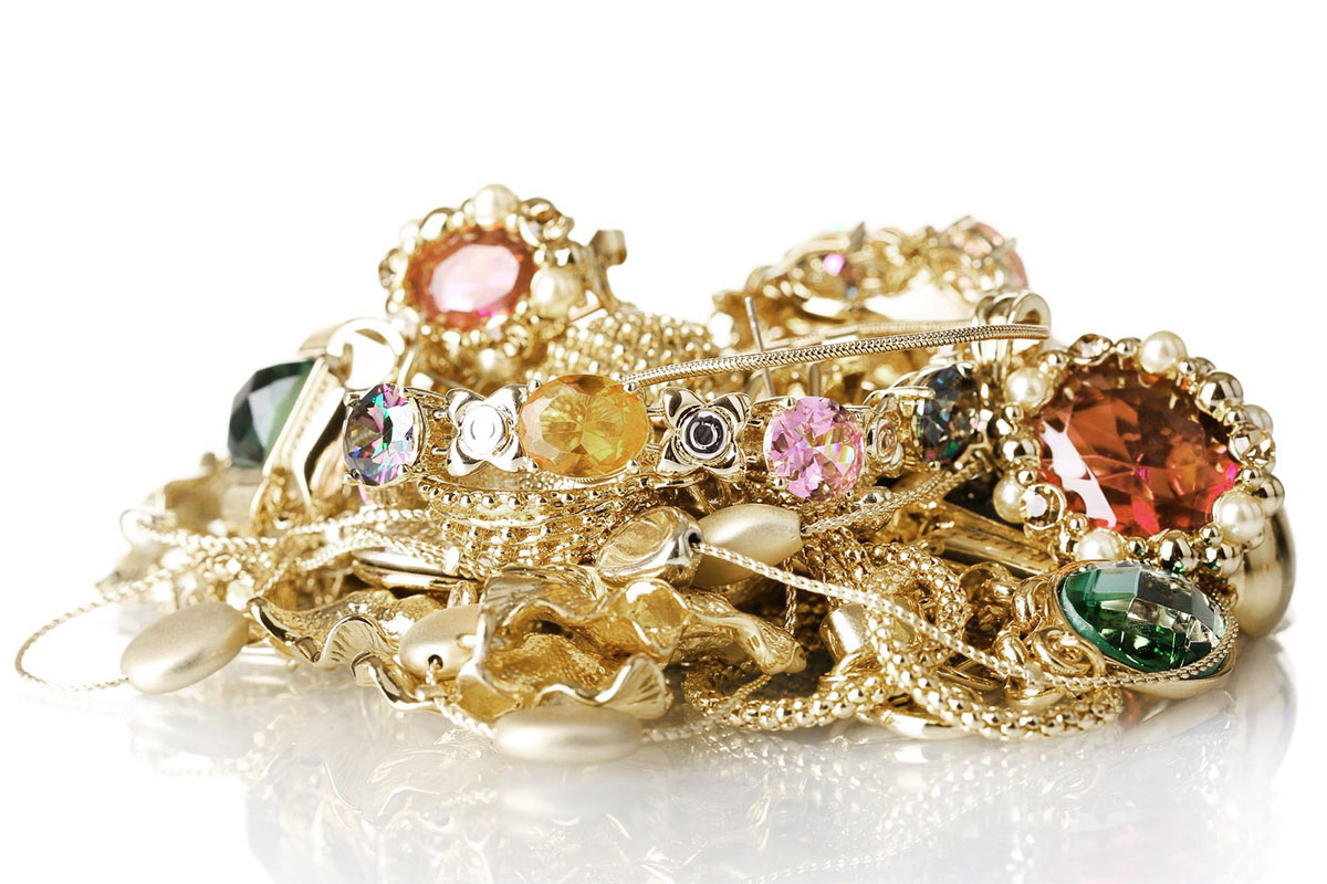 A pile of gold jewelry set with colored gemstones, including rings, brooches, and chains, against a white background