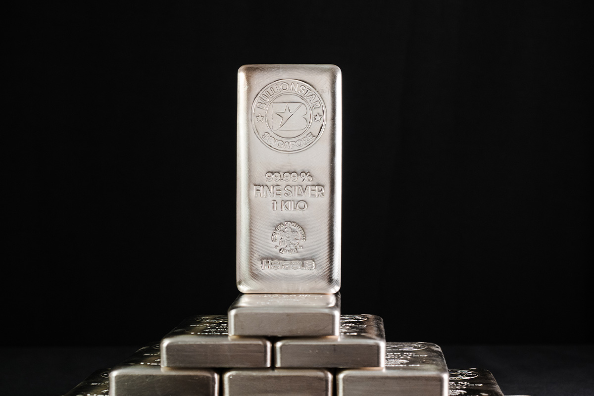 A BullionStar Singapore 1 kilo silver bar, stamped 99.99% fine silver with the Heraeus mint mark, standing on top of a stack of similar bars