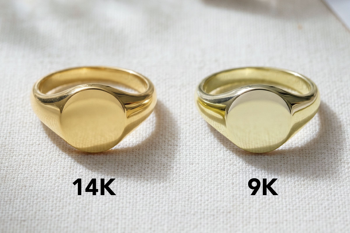 Side-by-side comparison of a 14K gold signet ring and a 9K gold signet ring on a fabric surface, labeled "14K" and "9K," showing the difference in gold color