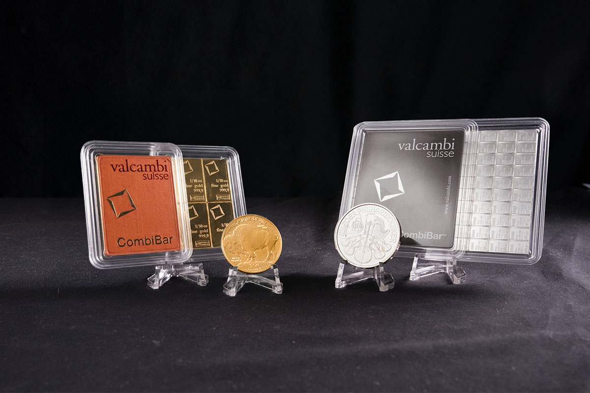 Gold and silver bullion bars and coins including Valcambi Suisse CombiBars, a gold buffalo coin, and a silver coin displayed on stands