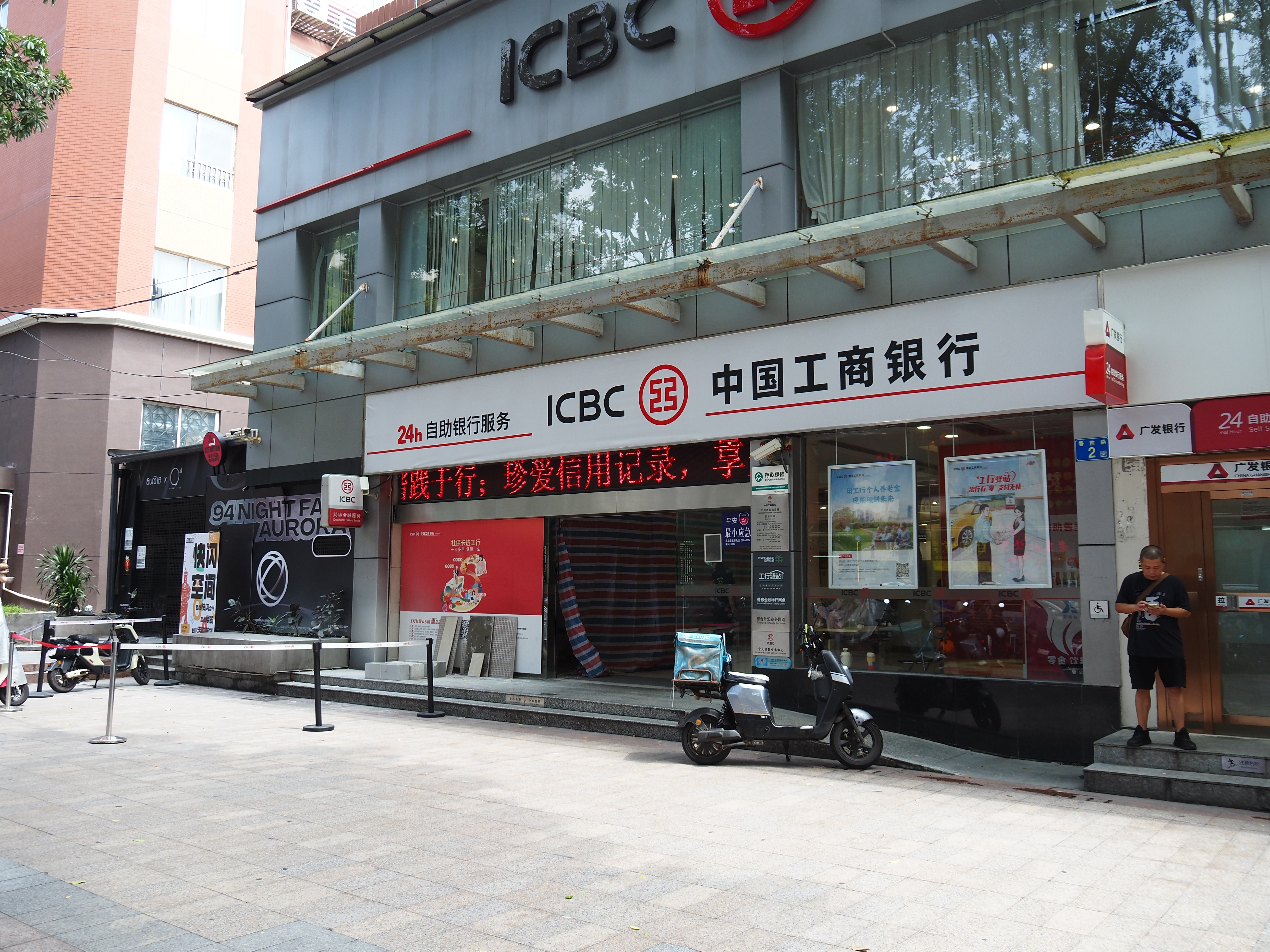 ICBC (Industrial and Commercial Bank of China) branch storefront in Guangzhou, China, with red and white signage, a digital scrolling display, and an electric moped parked outside
