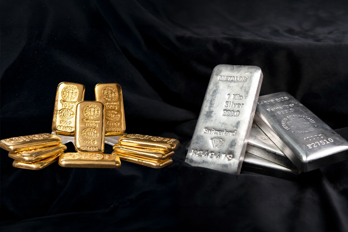 Stacked gold bars and silver bars, including Metalor and Heraseus branded silver bars, displayed together on black fabric