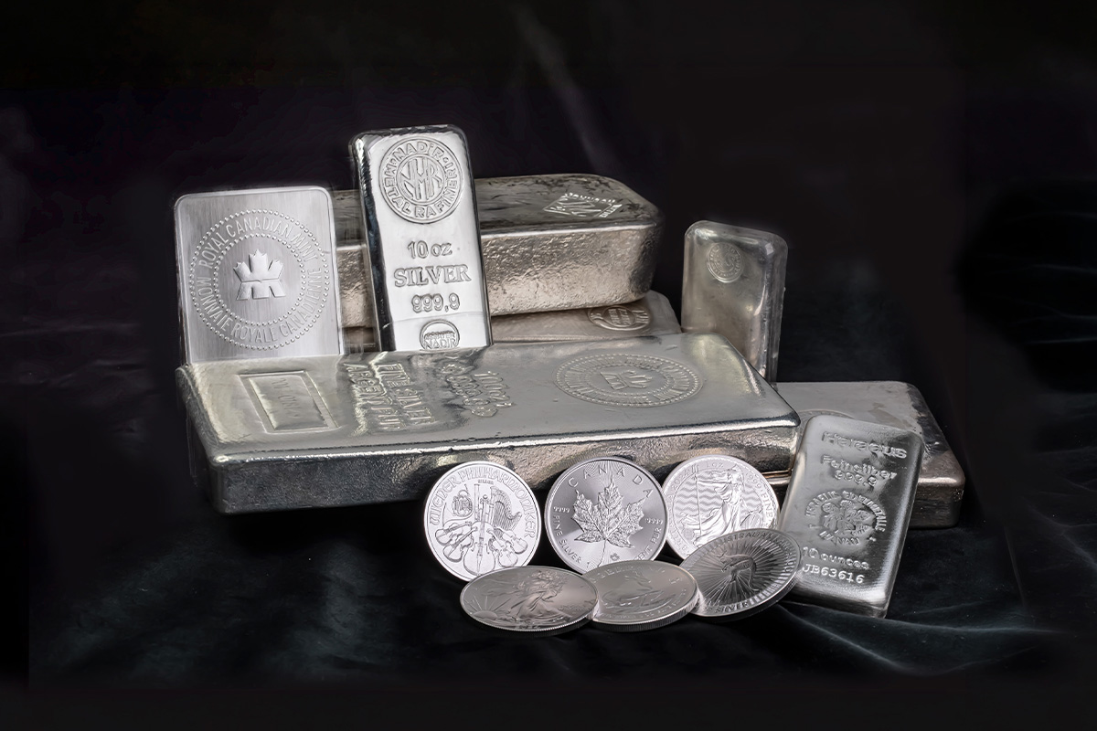 Stacked silver bars of varying sizes, including one marked Royal Canadian Mint and another stamped Heraeus 999.9, alongside silver coins with maple leaf and harp designs Title: Physical silver bars and coins together