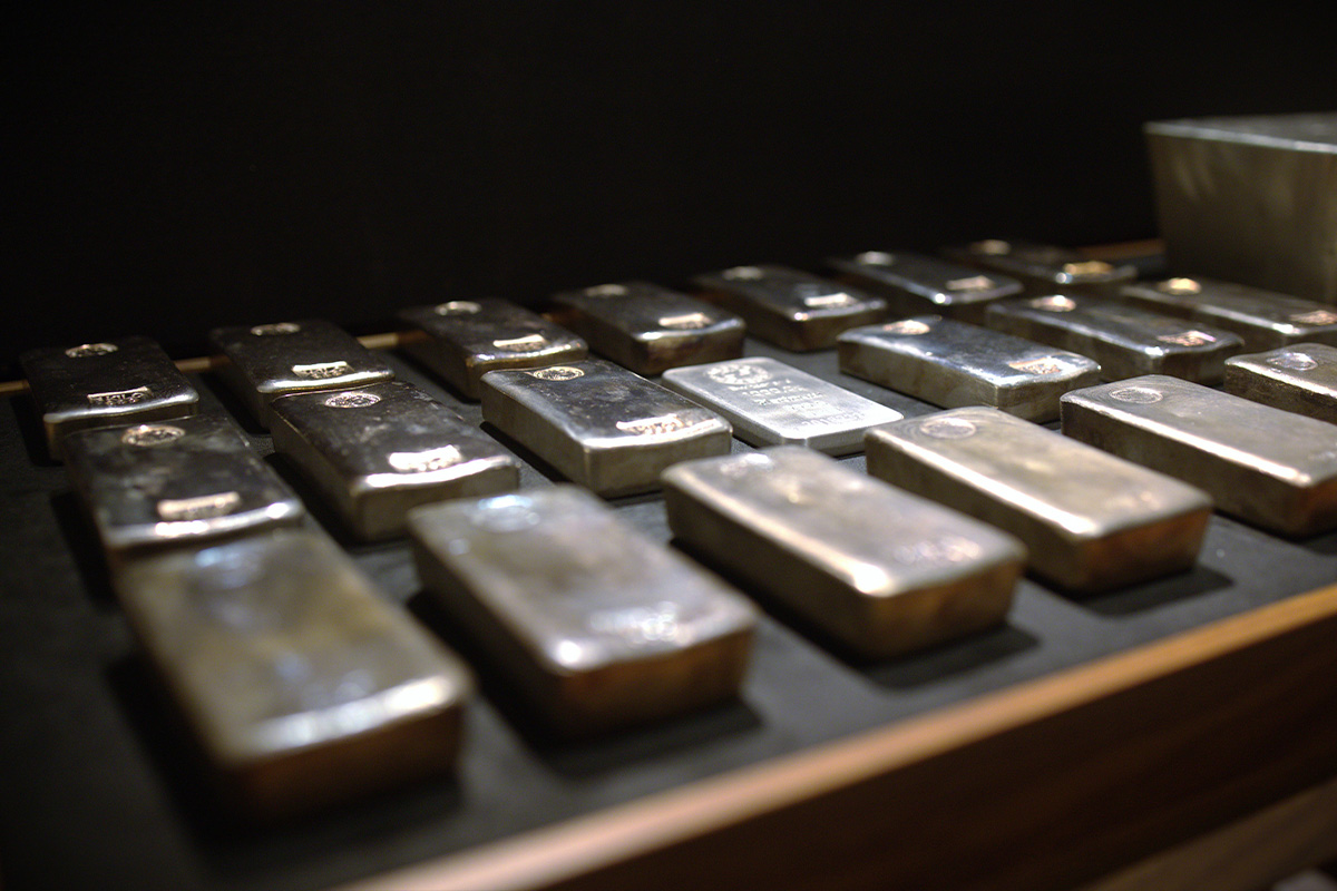 Rows of tarnished silver bars laid out on wooden shelving in a dimly lit storage setting