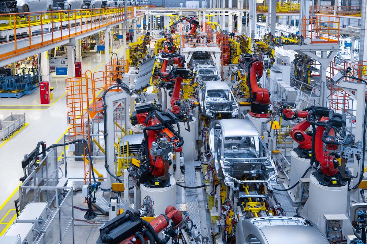 Overhead view of an automotive assembly line with red robotic arms welding car bodies on a factory production line