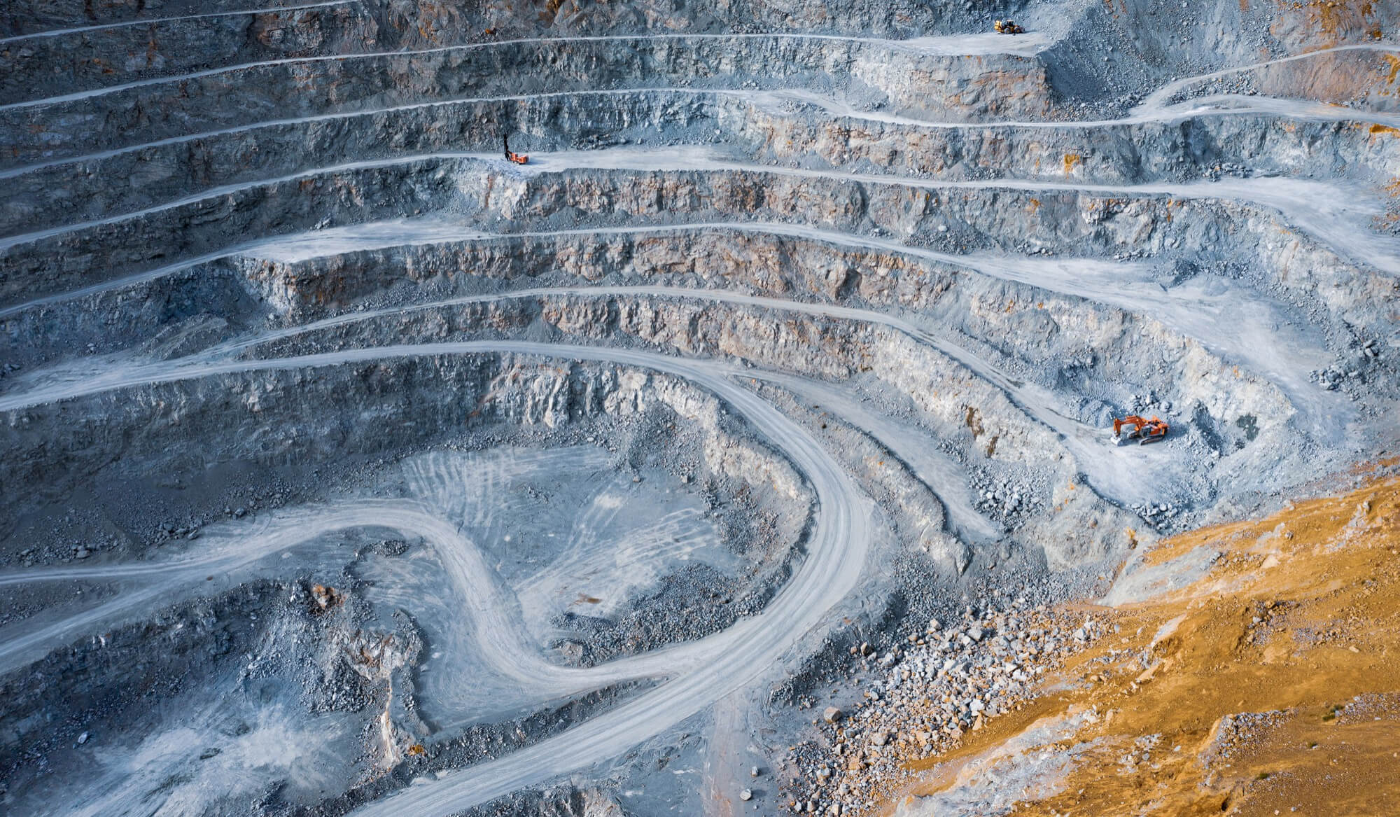 Aerial view of an open-pit platinum mine with terraced rock walls, switchback access roads, and excavation machinery
