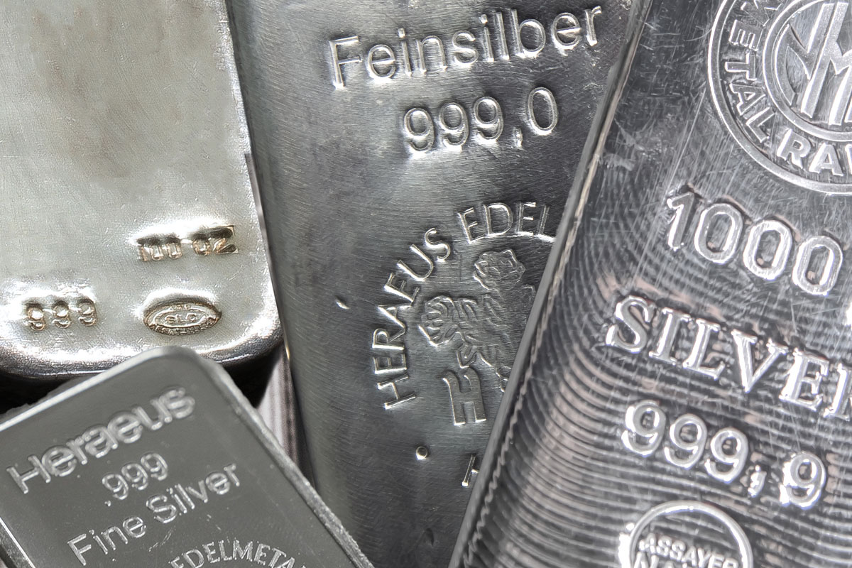 Close-up of stacked silver bars showing refiner stamps including "Feinsilber 999,0", "Heraeus Edelmetalle", "Heraeus .999 Fine Silver", "1000" with "SILVER 999,9", and a circular assayer stamp